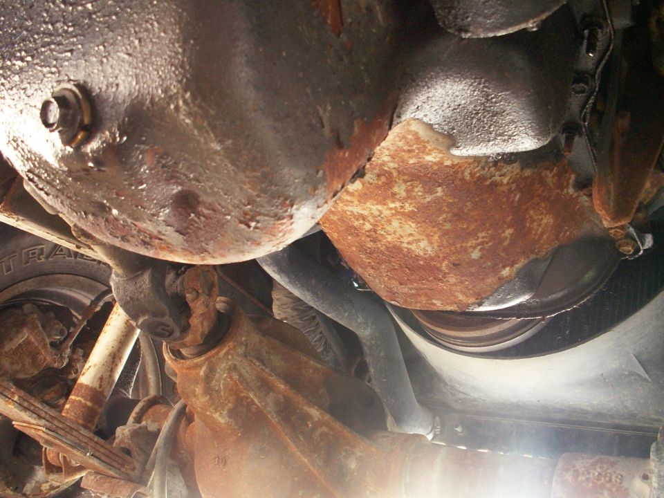 Underside view of rusty vehicle parts, including suspension and drivetrain components
