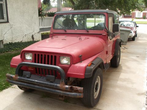 1988 Jeep YJ - A red Jeep Wrangler is parked on a concrete driveway next to another vehicle.