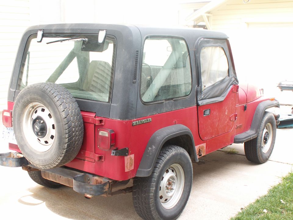 Red Jeep Wrangler with a black hardtop and spare tire on the rear, viewed from the rear three-quarter angle