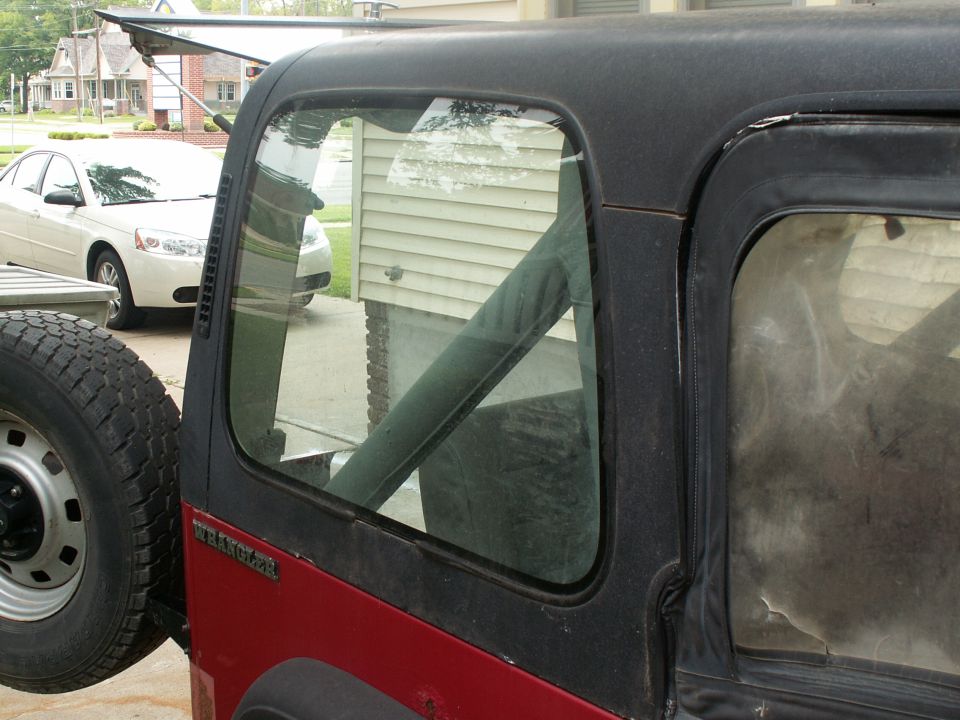 Red Jeep Wrangler with black soft top, spare tire mounted on rear, seen from the side