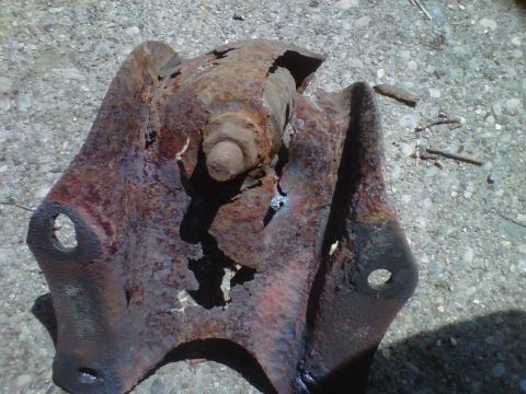 1995 Ford Bronco - Heavily rusted metal bracket with a large bolt and nut, likely a vehicle suspension component.