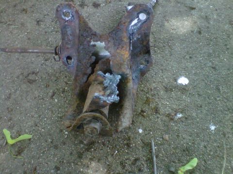 1995 Ford Bronco - A heavily rusted suspension component, showing signs of repair with welding, lies on the ground.
