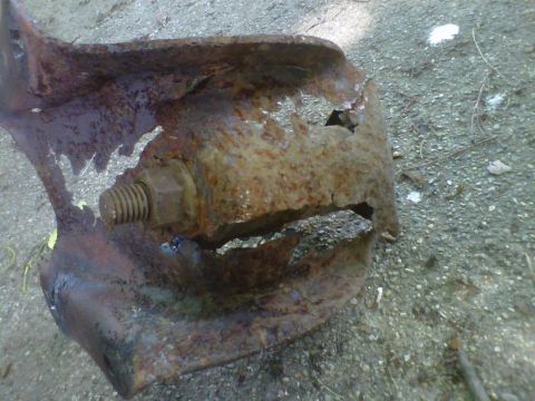 1995 Ford Bronco - A corroded metal bracket with a bolt is shown lying on the ground.