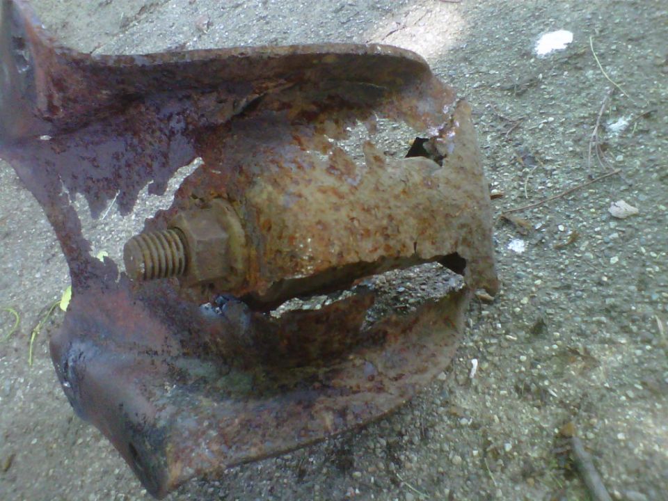 Heavily rusted metal bracket with a large bolt, showing significant corrosion and damage