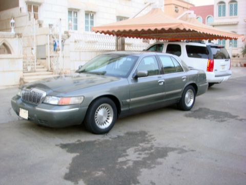 2001 Mercury Grand Marquis - A 2001 Mercury Grand Marquis is parked in front of a white SUV under a shaded canopy.