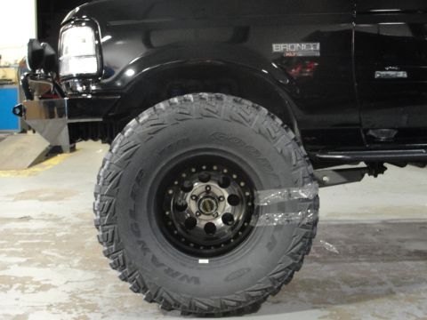 1995 Ford Bronco - Close-up of a black 1995 Ford Bronco's front tire and fender, with the "BRONCO XLT" badge visible.