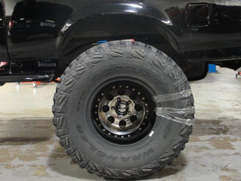1995 Ford Bronco - Close-up of a black SUV's tire and wheel, wrapped in plastic for protection.