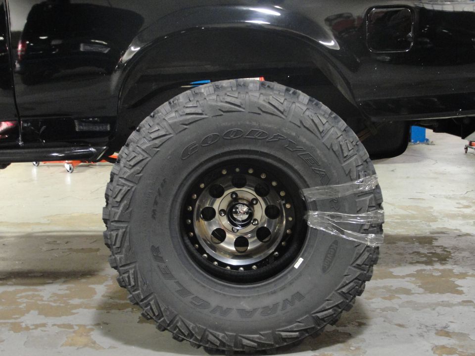 Black SUV tire with chrome beadlock wheel, wrapped in plastic