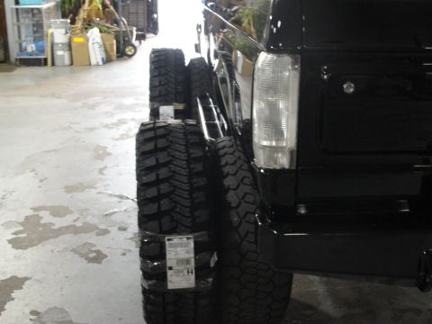 1995 Ford Bronco - Stack of off-road tires beside a black SUV's rear quarter panel.