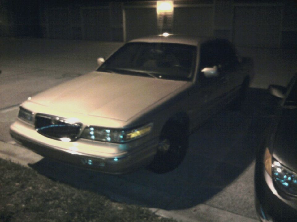 Silver sedan parked at night, front quarter view. Another car is partially visible on the right