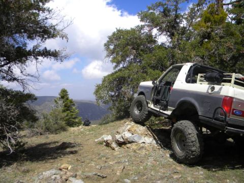 1991 Ford Bronco - This modified Ford Bronco navigates a challenging off-road trail amidst a picturesque mountainous landscape.