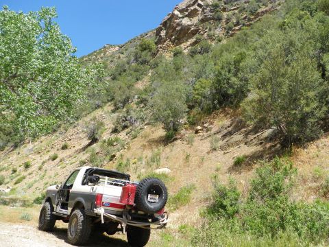 1991 Ford Bronco - 1991 Ford Bronco parked on a dirt path with a rocky mountain in the background.