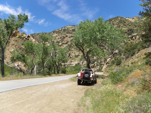 1991 Ford Bronco - A white SUV with a spare tire mounted on its rear is parked on the side of a road in a mountainous, tree-lined landscape.