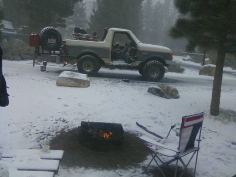 1991 Ford Bronco - A two-tone Ford Bronco sits in a snowy landscape next to a campfire and a folding chair.
