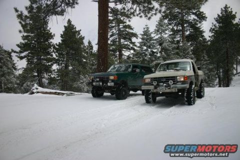 1991 Ford Bronco - Two SUVs, a 1991 Ford Bronco and a green SUV, are parked in a snowy forest landscape.