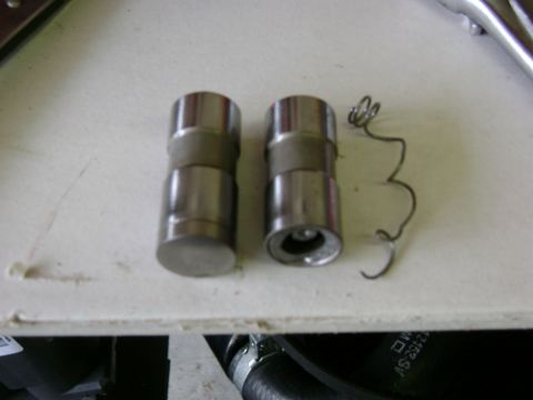 1972 Ford Ranchero - Two metal valve lifters and a coiled spring are shown on a white surface, likely engine components.