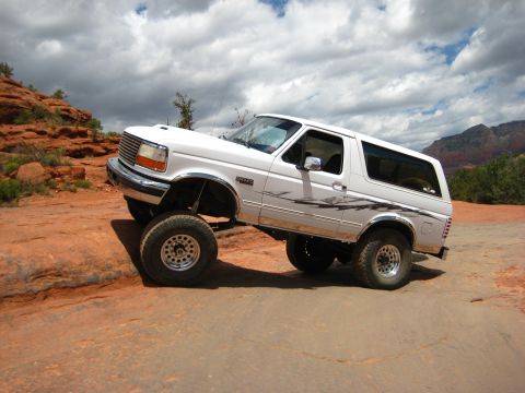 1996 Ford Bronco - A white Ford Bronco navigates a rocky trail under a cloudy sky.