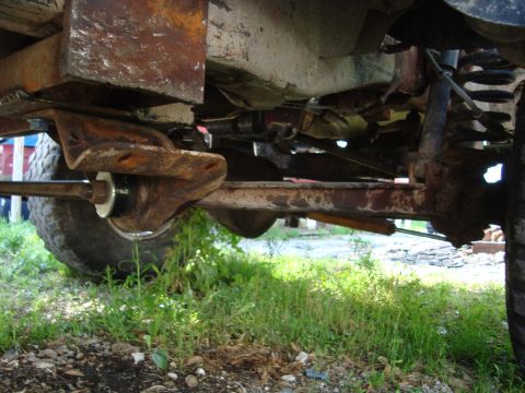 1999 Ford F-150 - The underside of a heavily rusted vehicle is visible, with focus on the suspension and drivetrain components.