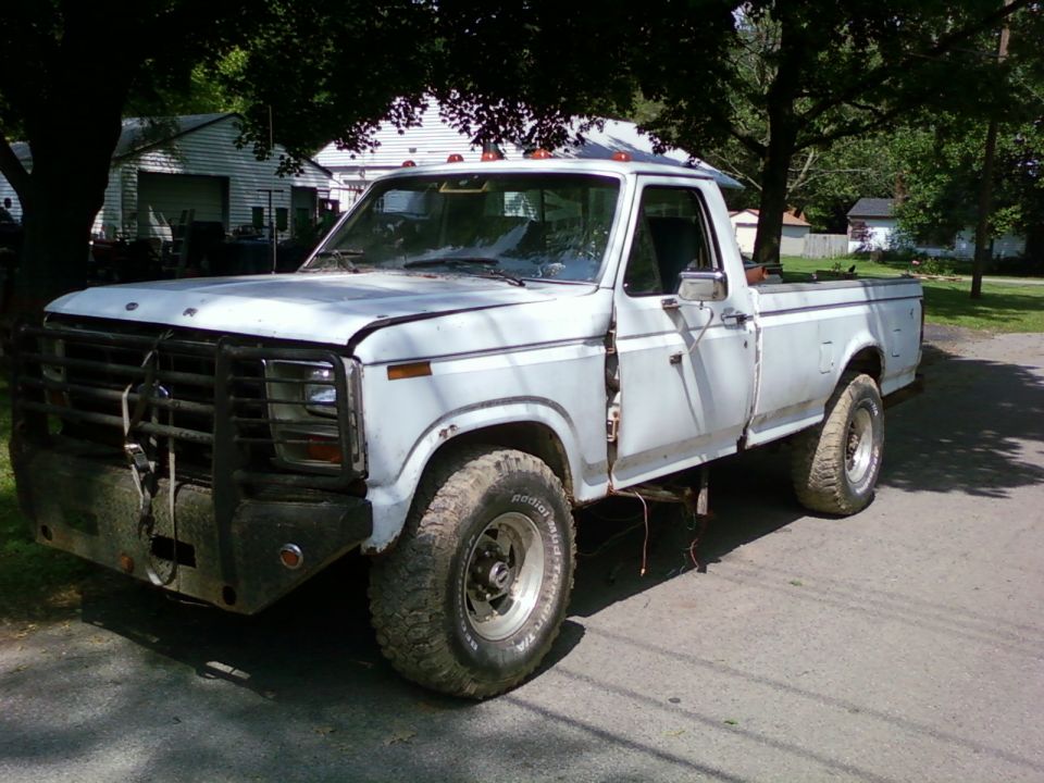 White pickup truck with bull bar and aftermarket wheels, 1980s body style