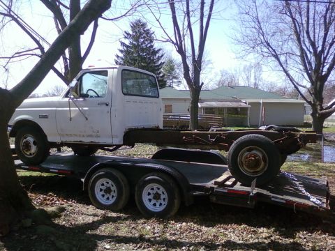 1989 Ford Bronco - A white truck chassis is loaded onto a trailer, viewed from the side.