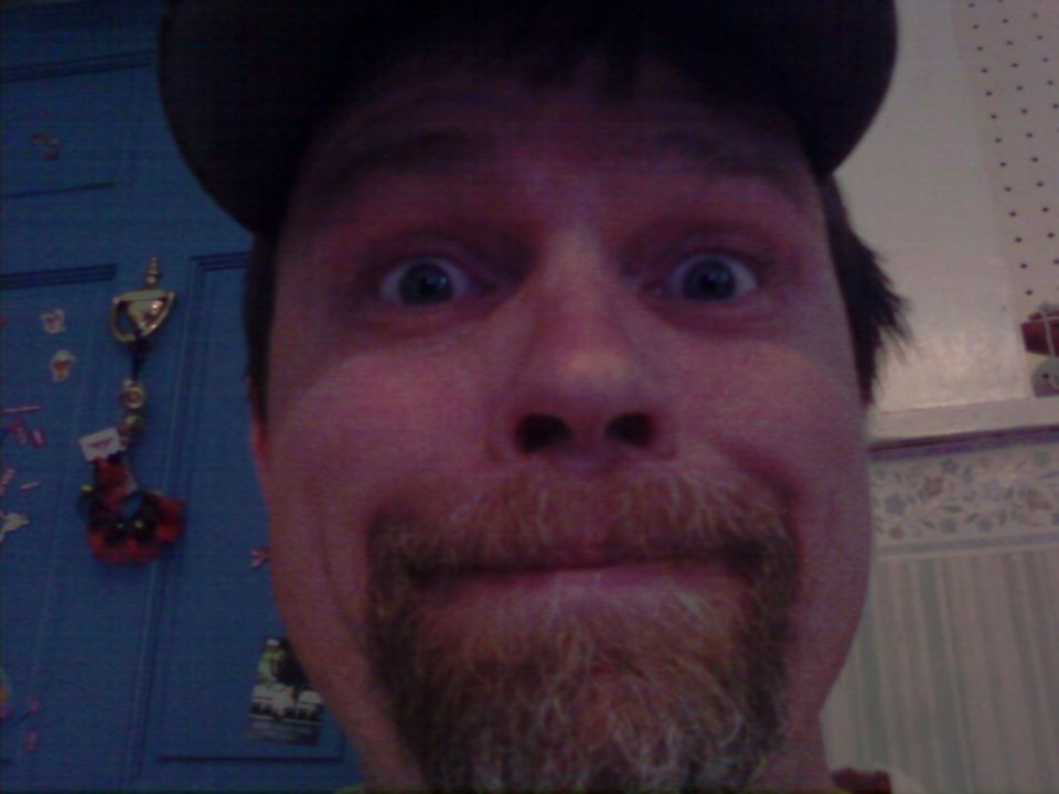 Man with wide eyes and a goatee wearing a dark baseball cap