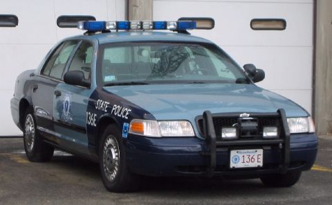 1998 Ford Crown Victoria - A Massachusetts State Police car is parked in front of a garage door, showing its front view and markings.