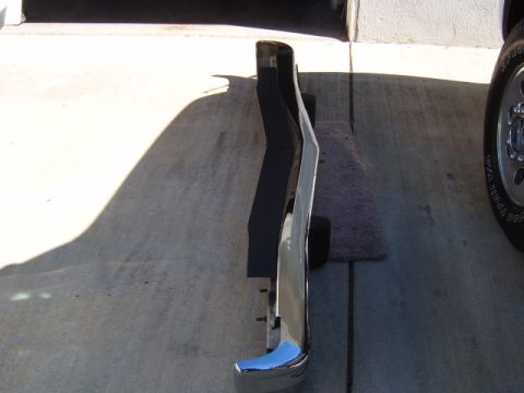 1973 Ford Ranchero - A chrome bumper with a black rubber strip is shown from the side on a concrete surface.