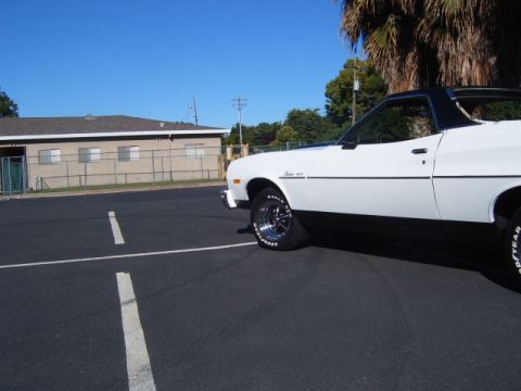 1973 Ford Ranchero - A white 1973 Ford Ranchero is parked in a lot, showing its side profile with black trim and a black vinyl roof.