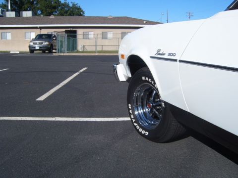 1973 Ford Ranchero - Close-up of a 1973 Ford Ranchero's side profile, showing the fender and wheel. A truck is visible in the background.