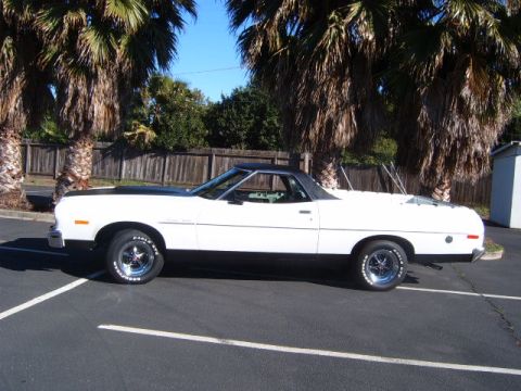 1973 Ford Ranchero - A white coupe utility with a black hood and roof is parked in a lot with palm trees overhead.