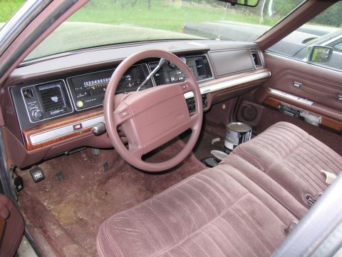 1991 Ford LTD Crown Victoria - The interior of a 1991 Ford Crown Victoria LTD features brown velour seats and a wood-grain dashboard with a prominent steering wheel.