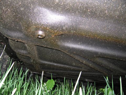 1991 Ford LTD Crown Victoria - The undercarriage of a vehicle is visible, covered in dirt and grime, with tall grass growing around it.