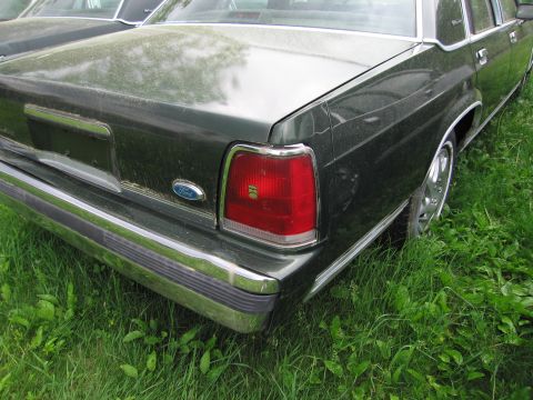 1991 Ford LTD Crown Victoria - Rear view of a dark green 1991 Ford Crown Victoria LTD parked in grass, showing its taillight and chrome bumper.