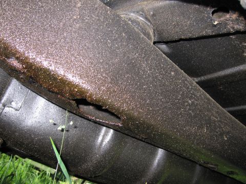 1991 Ford LTD Crown Victoria - Undercarriage view of a heavily rusted vehicle frame with a hole in the metal.