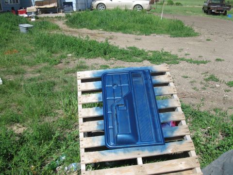 1977 Ford F-250 - A blue door panel is drying on a wooden pallet in a grassy yard.