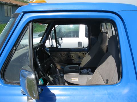 1977 Ford F-250 - Interior view of a blue truck, showing the driver's seat, steering wheel, and a glimpse of another vehicle outside.