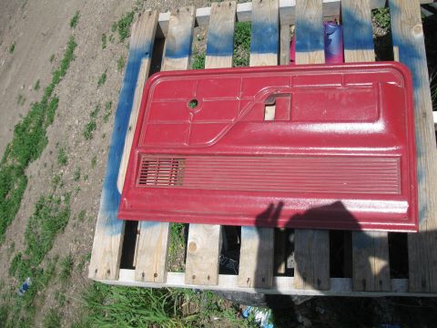 1977 Ford F-250 - Red truck door panel with speaker grille, resting on wooden pallets outdoors.