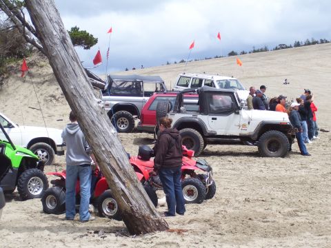 1991 Ford Bronco - A group of people and various off-road vehicles gather on a sandy dune landscape.
