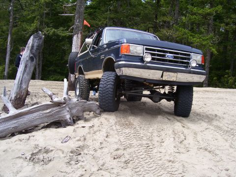 1991 Ford Bronco - This lifted 1991 Ford Bronco is shown off-roading on a sandy beach with a forest backdrop.