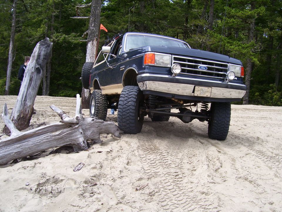 1991 Ford Bronco with lifted suspension and large tires on a sandy beach with trees in the background