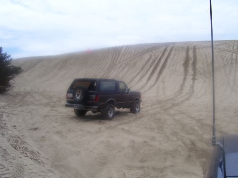 1991 Ford Bronco - A black 1991 Ford Bronco navigates a sandy terrain with tire tracks marking the dune.