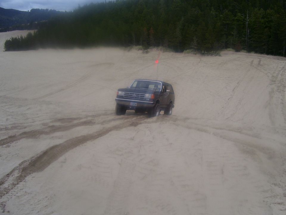 1991 Ford Bronco driving on sand dunes with trees in background
