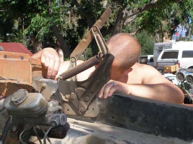 Man working on a rusty 1969 Ford F-250 engine bay, showing brake master cylinder and linkage