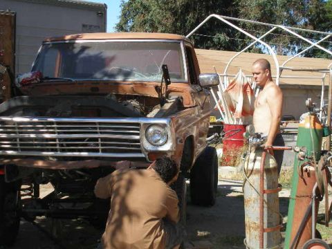 1969 Ford F-250 - Two men work on the front end of a rusty pickup truck outdoors.