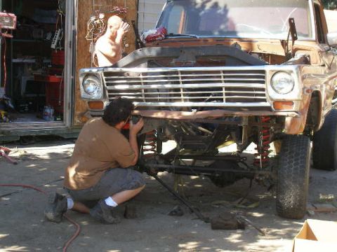 1969 Ford F-250 - A person kneels to work on the front end of a vintage Ford truck, with the hood open and grille exposed.