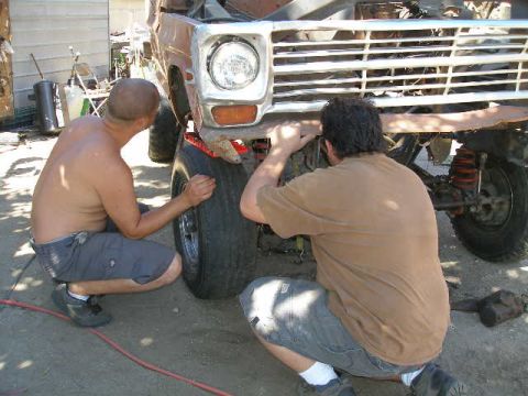 1969 Ford F-250 - Two men work on the front end of a truck, which has a chrome grille and round headlights.