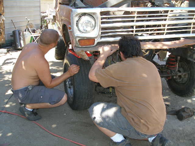 Truck front end with chrome grille and round headlights, being worked on by two men