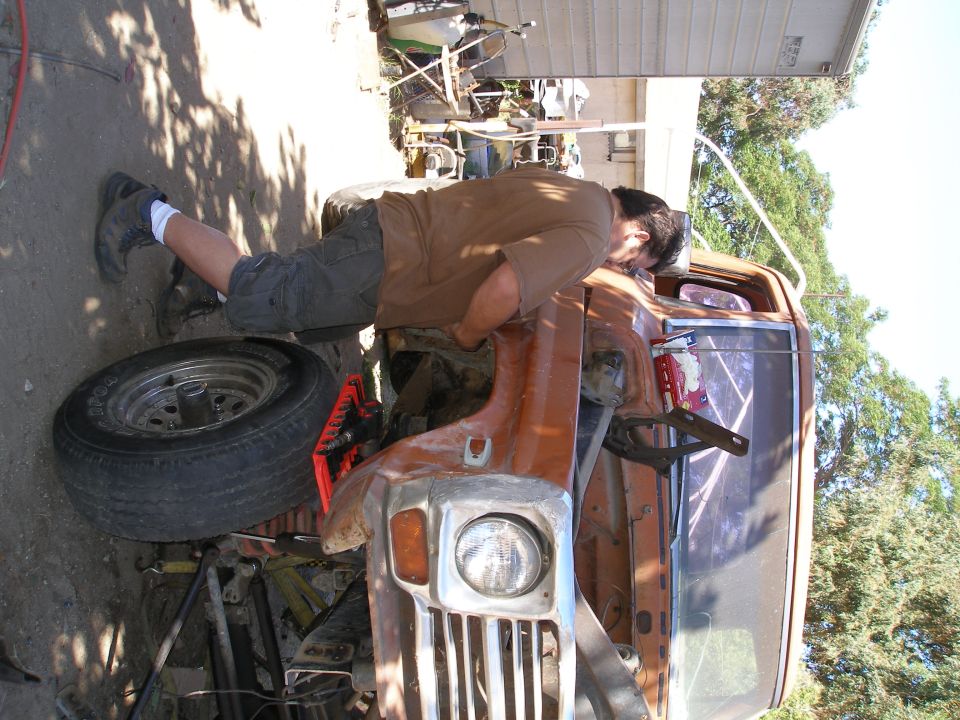 Man leaning into the engine bay of a rusty 1970s pickup truck
