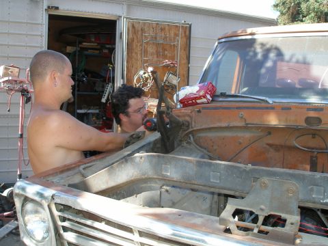 1969 Ford F-250 - Two men are working on the engine bay of an old truck, with tools and parts scattered around.