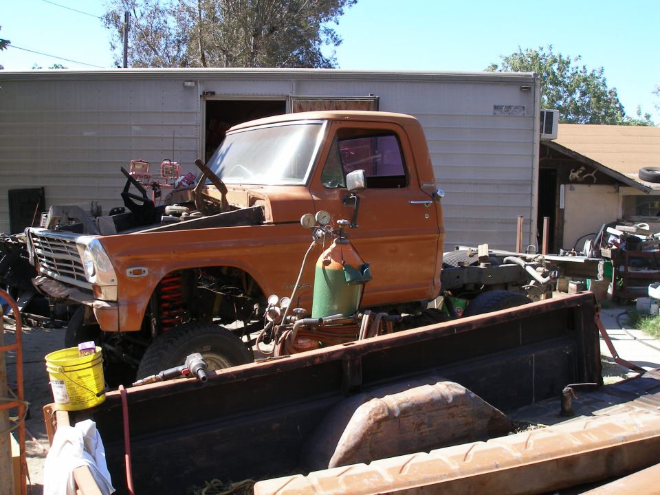 Orange 1967 Ford F-series truck chassis with hood removed, showing engine bay and front suspension